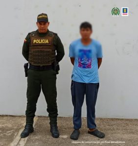 En la imagen se ve una persona detenida en custodia de un integrante de la Policía Nacional.