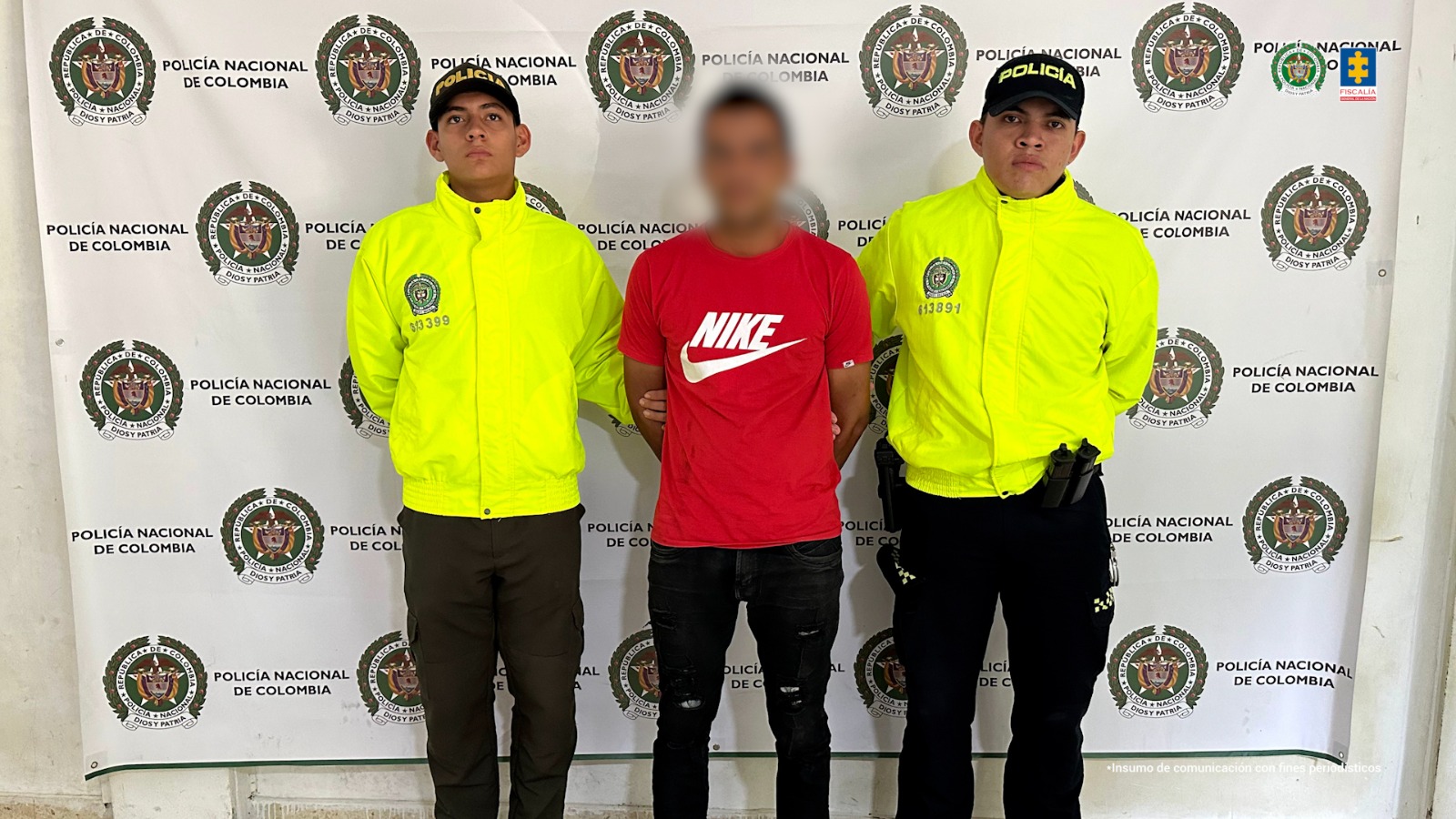 en la imagen se ve una persona detenida bajo custodia de dos integrantes de la Policía Nacional.