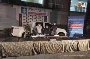 en la imagen se ven dos personas detenidas bajo custodia del Ejército y el CTI de la Fiscalía. Detrás suyo backings institucionales y delante de ellos una mesa con material de guerra incautado.