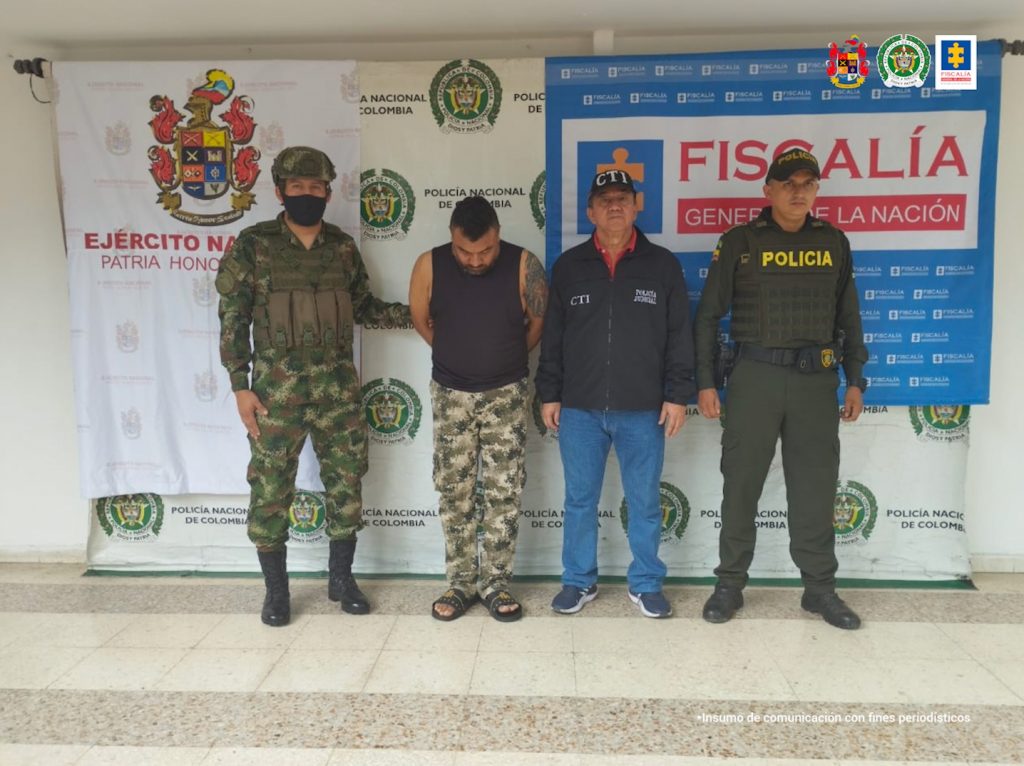 en la imagen se ve una persona detenida bajo custodia de integrantes del CTI de la Fiscalía, Gaula Ejército y Policía Nacional. Detrás suyo backings institucionales.