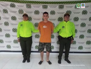 en la imagen se ve una persona detenida bajo custodia de dos integrantes de la Policía Nacional.
