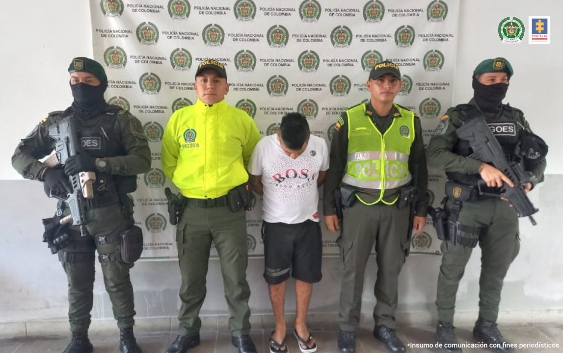 En la foto se ven cuatro funcionarios de la Policía Nacional con un detenido y al fondo un backing de la misma institución.