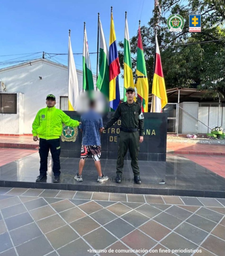 El capturado se encuentra de espaldas y en custodia por dos uniformados de la Policía Nacional.