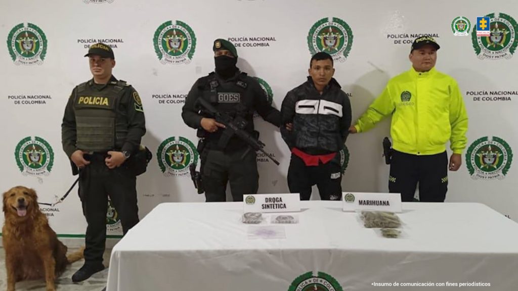 en la imagen se ve una persona detenida bajo custodia de tres integrantes de la Policía Nacional y un perro. Frente a ellos una mesa con varias sustancias incautadas.