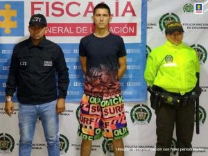 En la imagen se ve una persona detenida bajo custodia del CTI y la Policía Nacional. Detrás suyo un backing de la Fiscalía.