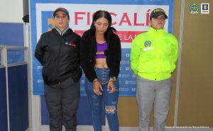 En la imagen se ve una mujer detenida bajo custodia de la Policía y el CTI. Detrás suyo un backing de la Fiscalía.