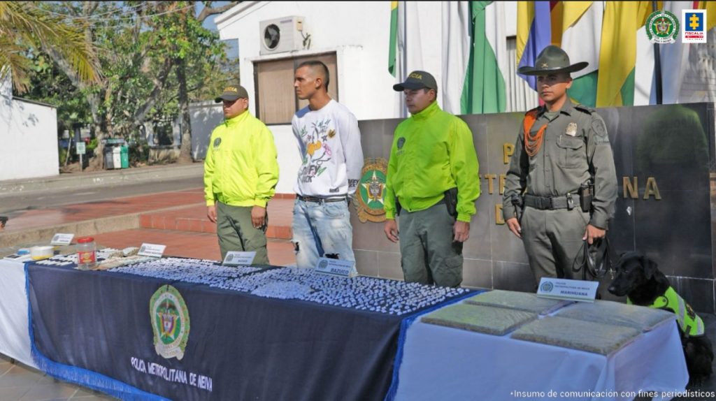 en la imagen se ve un hombre detenido bajo custodia de dos integrantes de la Policía Nacional. Frente a él una mesa con sustancia estupefaciente y otros elementos incautados en un allanamiento.