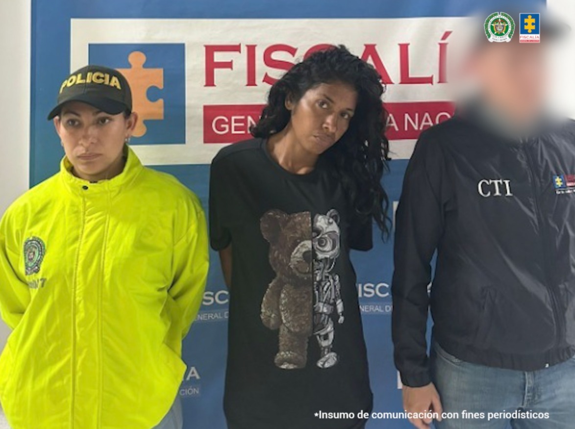 Se ve una mujer detenida bajo custodia de un investigador del CTI y de la Policía Nacional. Detrás un backing institucional.