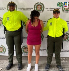 en la imagen se ve una mujer detenida bajo custodia de dos integrantes de la Policía Nacional. Detrás suyo un backing institucional.