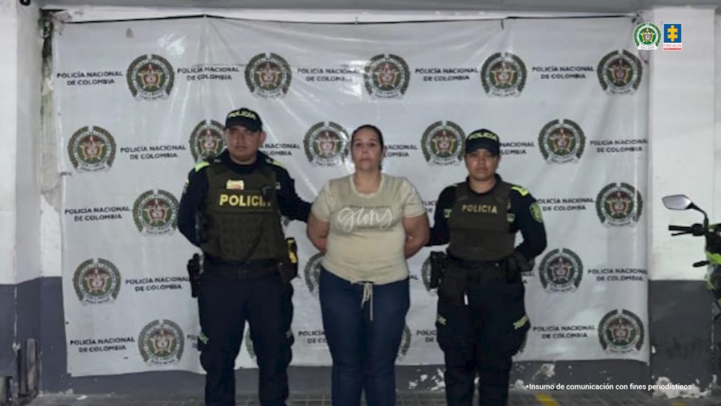 en la imagen se ve una mujer detenida bajo custodia de la Policía Naciona, detrás suyo un backing institucional.