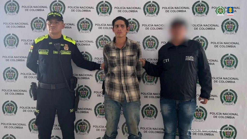 en la imagen se ve una persona detenida bajo custodia de un investigador del CTI y de la Policía Nacional. Detrás suyo, un backing institucional.