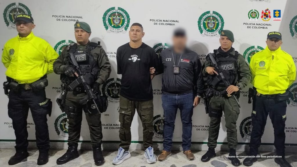 en la imagen se ve una persona detenida bajo custodia de investigadores del CTI e integrantes de la Policía Nacional. Detrás suyo un backing institucional.