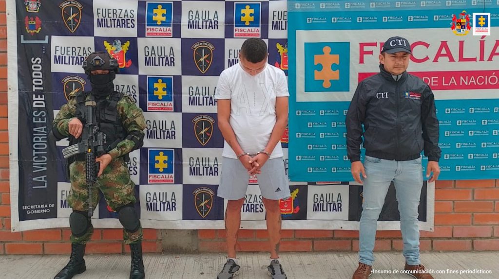 En la imagen se ve una persona detenida bajo custodia de un investigador del CTI y el Ejército. Detrás suyo backings institucionales.