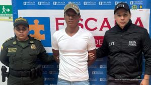 En la imagen se ve una persona detenida bajo custodia de un integrante del CTI de la Fiscalía y otro de la Policía Nacional. Detrás suyo un backing institucional.