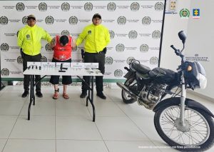 Los capturados aparecen junto a una mesa donde se exhiben los elementos incautados como drogas ilícitas, armas de fuego y traumática, dinero y elementos para la dosificación de las sustancias.