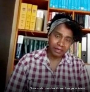 En la imagen se ve a la exministra Maria Isabel Urrutia con una paloleta azul en la cabeza y una blusa a cuasdros rojo con blanco. De fondo un mueble con varios libros.