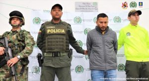 en la imagen se ve una persona detenida bajo custodia de la Policía y el CTI. Detrás suyo un backing institucional.