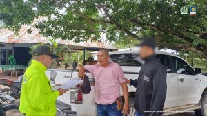 en la imagen se ve una persona detenida bajo custodia de un integrante de la Policía Nacional y un investigador del CTI. Detrás suyo un backing institucional.
