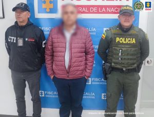 Fiscal Martha Mancera, Martha Mancera, Fiscal Mancera capturados de frente custodiados por investigador del CTI de la Fiscalía y Policía. Detrás banner de Fiscalía.