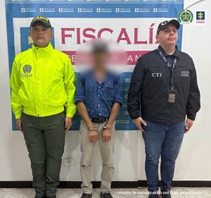  capturados en imágenes individuales custodiados por un investigador del CTI de la Fiscalía y un policía. Detrás banner de la Fiscalía.