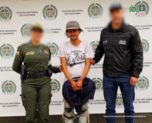 Luis Fernando Hurtado Montes en la foto acompañado de una funcionaria de la Policía Nacional y otro del CTI, detrás un pendón con logos de la Policía Nacional.