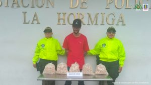 En la imagen se ve una persona detenida bajo custodia de dos integrantes de la Policía Nacional. Delante suyouna mes a con sustancia estupefaciente incautada.