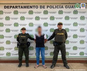  capturado de frente esposado, manos atrás, custodiado por dos uniformados de la Policía Nacional. Detrás banner de la Policía Nacional.