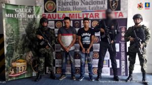 capturados sentados en el borde de un camino custodiados por militares.