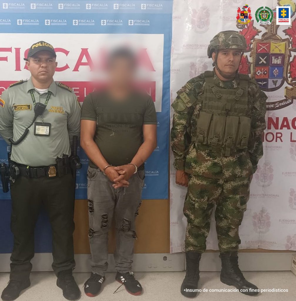 En la imagen se ve una persona detenida bajo custodia de un uniformado de la Policía Nacional y el Ejército. Detrás de ellos un backing de la Fiscalía y otro del Ejército.