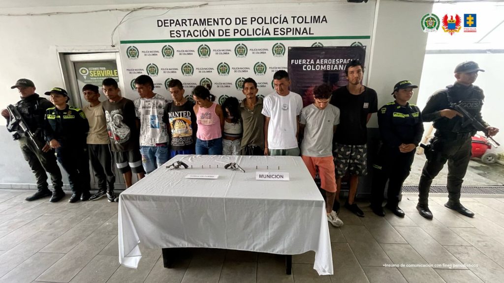en la imagen se ve un grupo de personas detenidas bajo custodia de integrantes de la Policía Nacional. Detrás suyo un backings institucionales.
