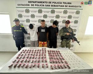 en la imagen se ven tres personas detenidas bajo custodia de integrantes de la Policía y el Ejército. Delante suyo una mesa con elementos incautados y detrás un backing institucional.