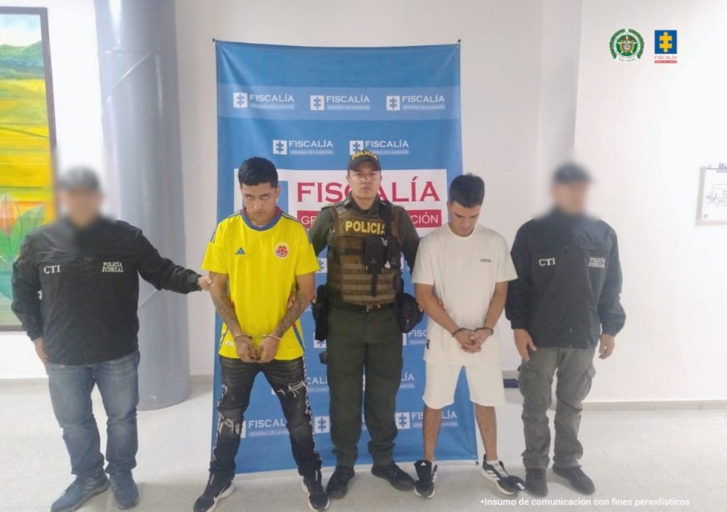 En la imagen se ven dos personas detenidas bajo custodia del CTI y la Policía Nacional, detrás suyo un backing institucional.