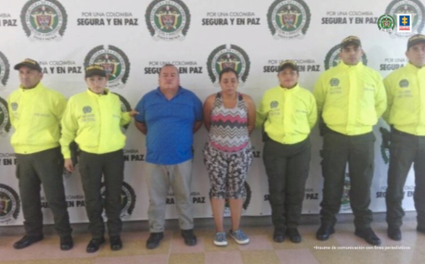 En la foto se ve una pareja detenida bajo la custodia de varios uniformados de la Policía Nacional. Detrás suyo un backing de la institución.