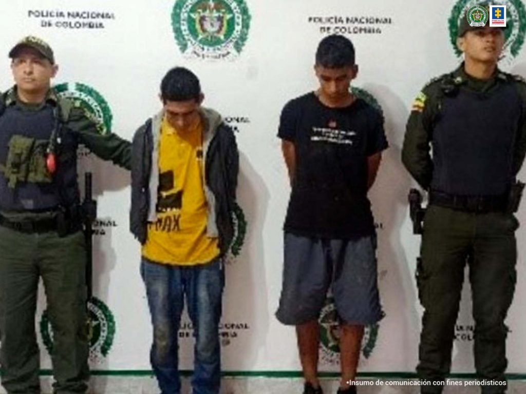 En la imagen se ven detenidas dos personas bajo custodia de la Policía. Detrás suyo un backing de la institución.