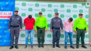  en la imagen se ven dos personas detenidas bajo custodia de servidores de la Policía y CTI. Detrás suyo backings institucionales.