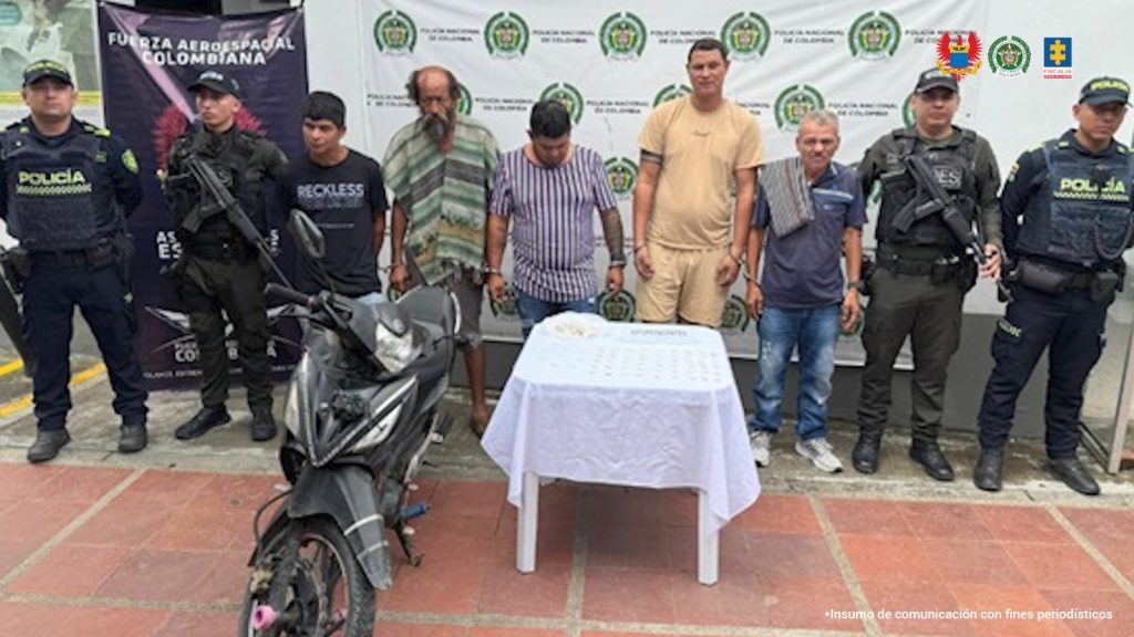 en la imagen se ven varias personas detenidas bajo custodia de integrantes de la Policía Nacional. Detrás un backing institucional.