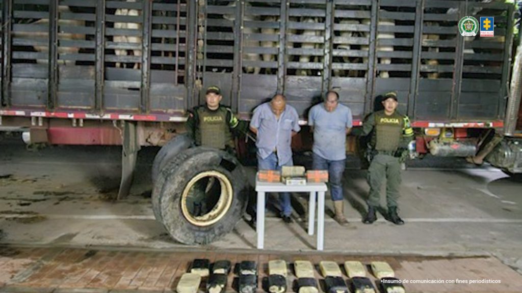 En la imagen se ven dos hombres detenidos bajo custodia de la Policía. Frente a ellos una mesa con elementos incautados y detrás un camión inmovilizado.