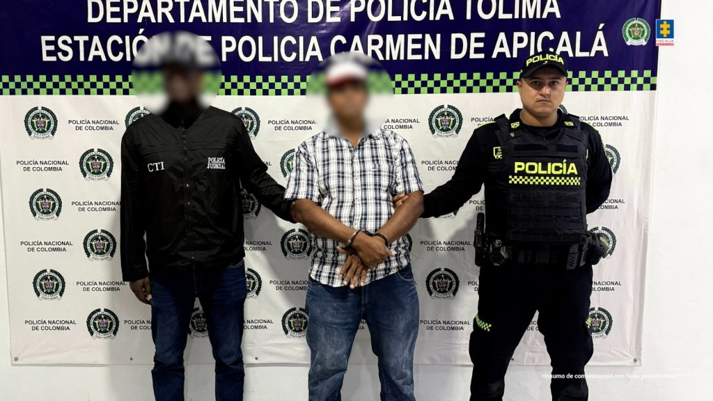 en la imagen se ve un hombre detenido bajo custodia de un investigador del CTI y de un integrante de la Policía Nacional.  Detrás suyo un backing institucional.