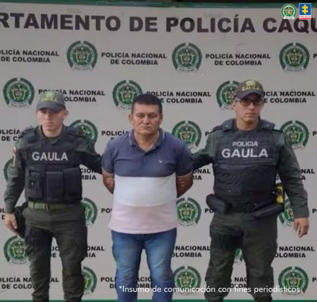 En la imagen se ve una persona detenida bajo custodia de dos integrantes de la policia.