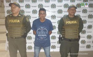 En la imagen se ve una persona detenida bajo custodia de dos integrantes de la Policía Nacional.