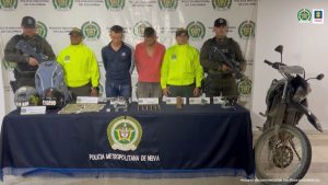 En la imagen se ven dos personas detenidas bajo custodia de la Policia Nacional. Detrás suyo backings institucionales.