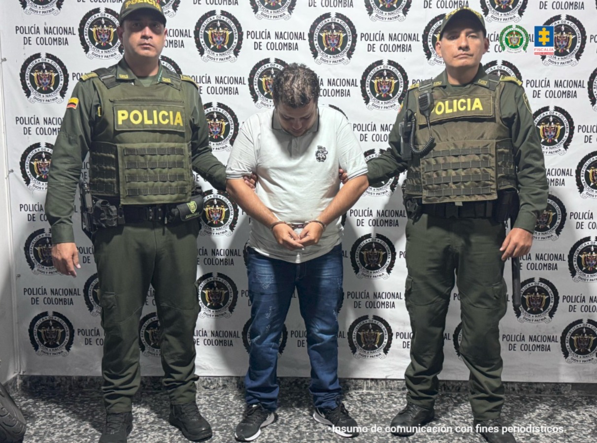 en la imagen se ve una persona detenida bajo custodia de dos integrantes de la Policía Nacional.
