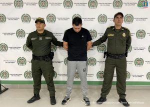 Los captureados aparecen custodiados por uniformados de la Policía y detrás de ellos un pebndón institucional.