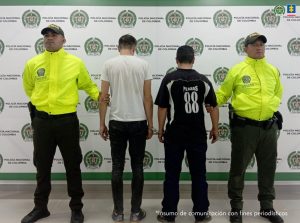 Los captureados aparecen custodiados por uniformados de la Policía y detrás de ellos un pebndón institucional.