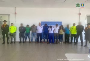 en la imagen se ven varias personas detenidas bajo custodia de la Policía Nacional. Detrás suyo un backing institucional.