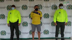 en la imagen se ve una persona detenida bajo custodia de dos integrantes de la Policía Nacional.