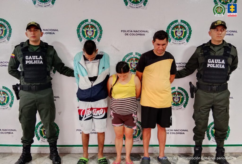 En la imagen se ven tres personas detenidas bajo custodia de dos uniformados del Gaula de la Policía. Detrás suyo un backing institucional.