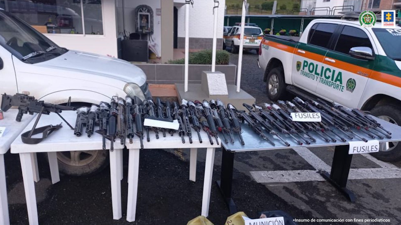En la fotografía se observan 7 mesas en la que están colocados fusiles 5.56, una ametralladora M.60, pistolas, granadas, explosivos y dos galones con municiones.