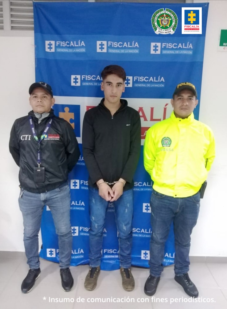 El capturado está esposado con sus manos al frente y está custodiado por un servidor del CTI de la Fiscalía y un uniformado de la Policía Nacional.