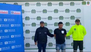 Asegurados dos hombres investigados por homicidio en Caquetá En la imagen se ve una persona detenida bajo custodia de un investigador del CTI y de la Policía. Detrás suyo backings institucionales.